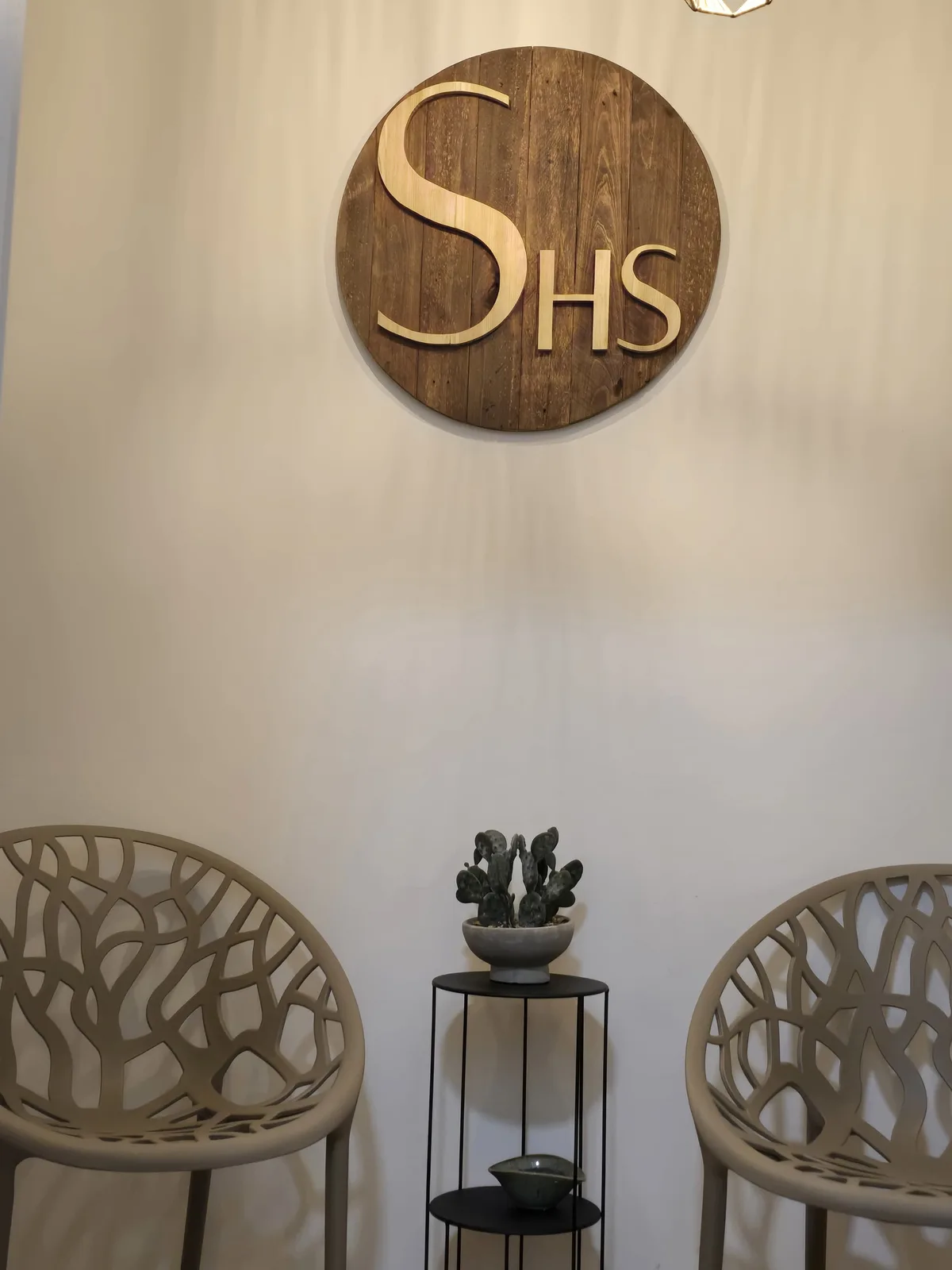Recepción de Simone Head Spa con el emblema de madera, dos sillas y una planta.